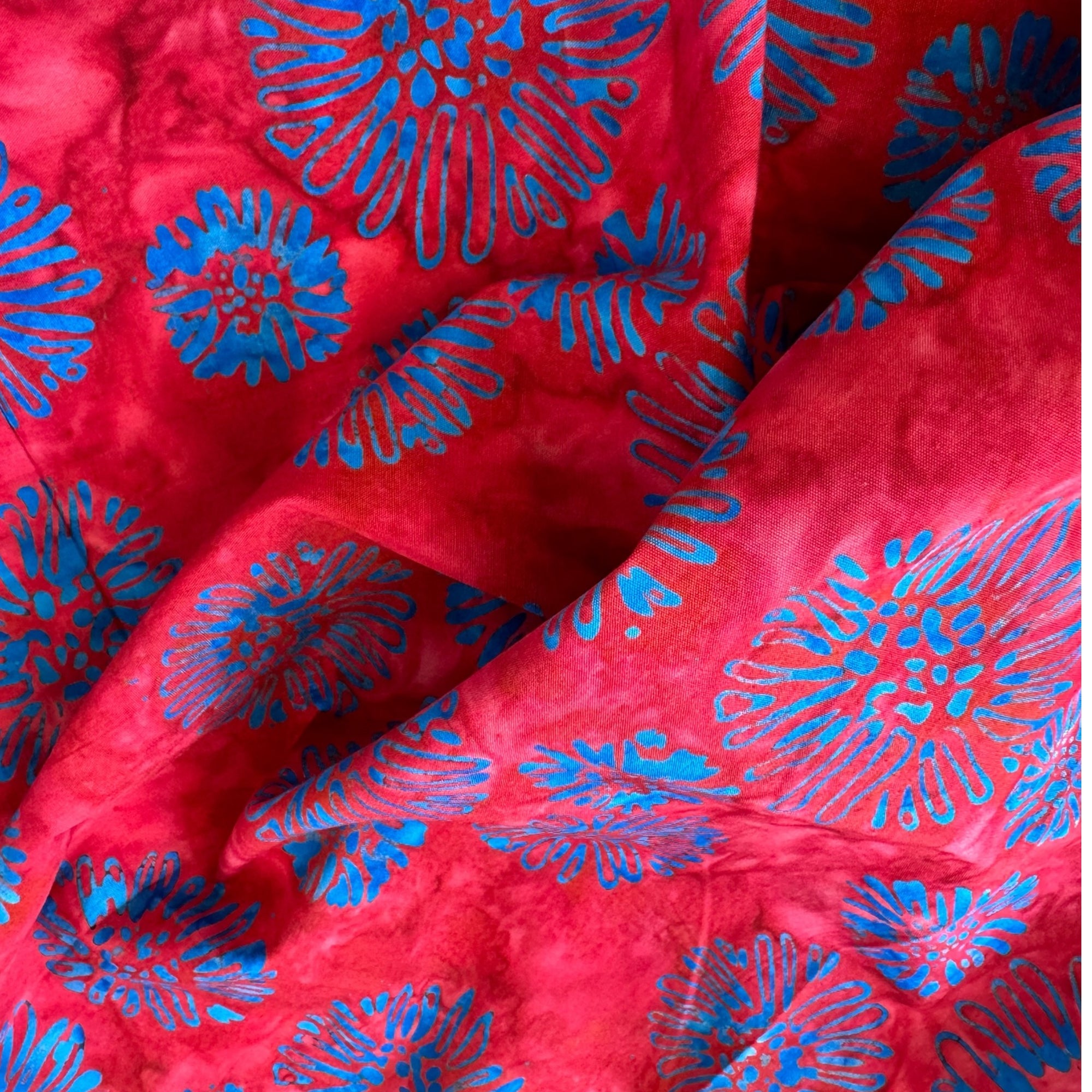 Tela batik flores crisantemo azul turqués sobre rojo carmín