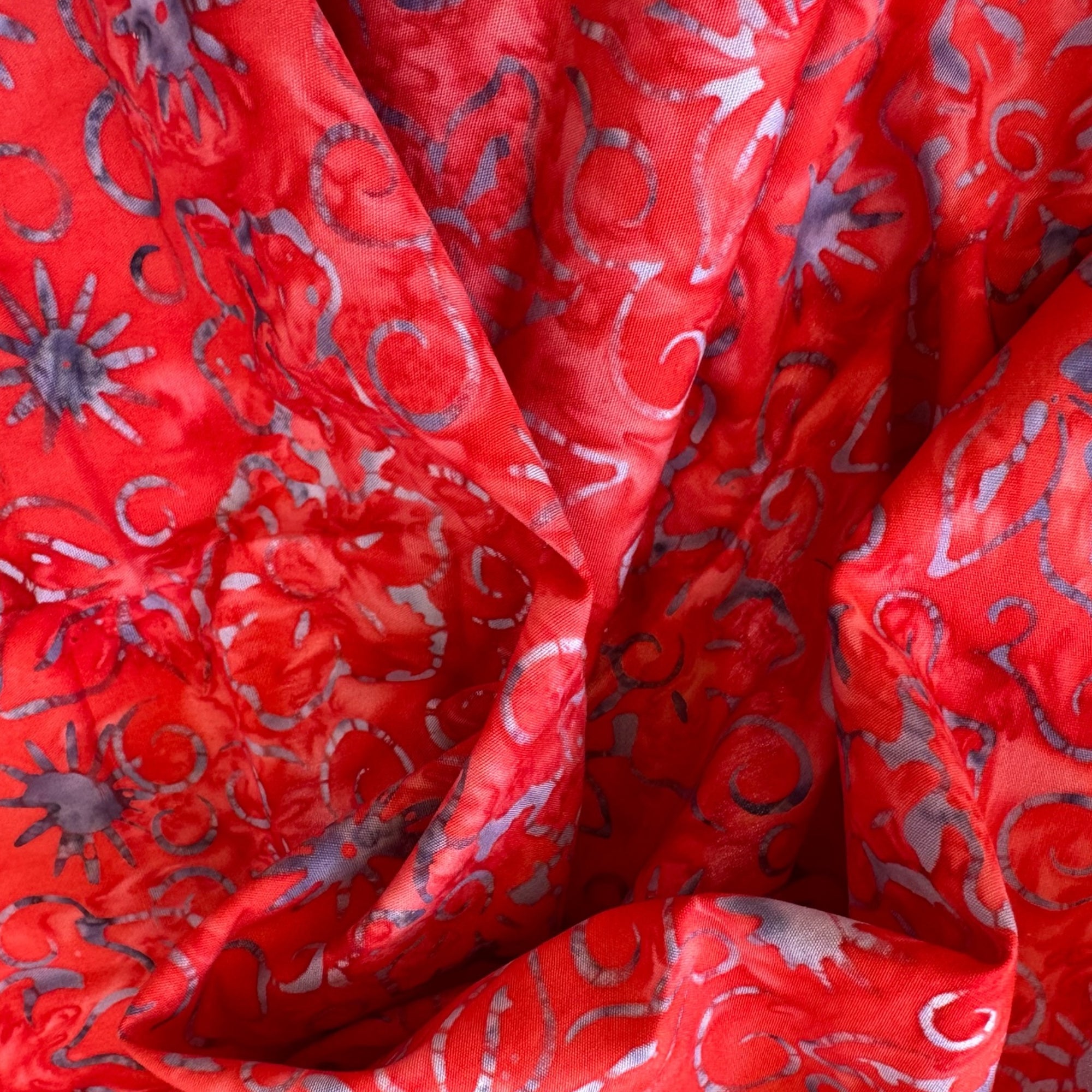 Tela batik soles y arabescos lila sobre rojo vivo